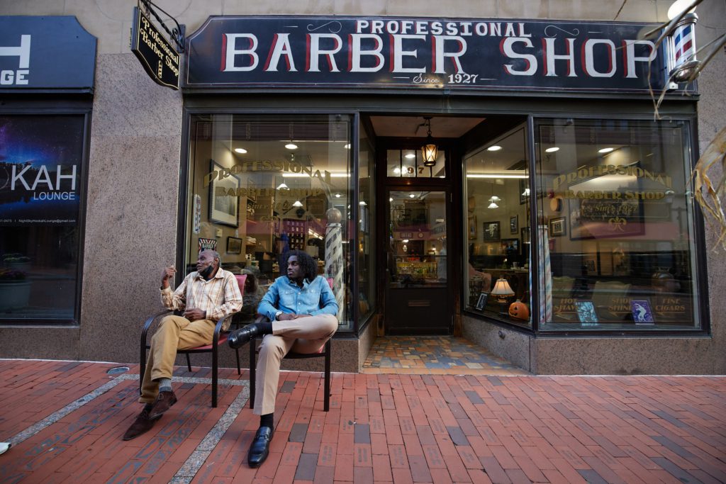 Two men sitting outside the barber shop on Pratt Street