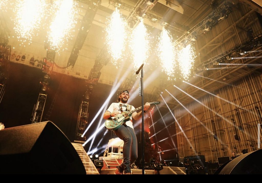 Thomas Rhett performing on stage with lights and sparklers behind him