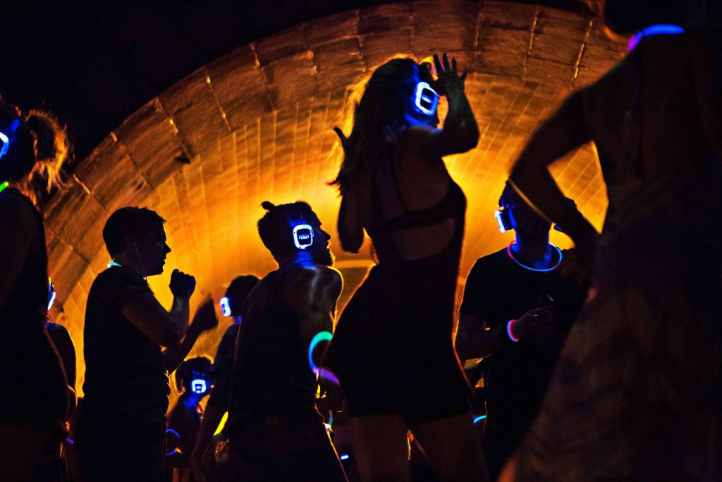 People dancing in a dark tunnel during an evening silent disco