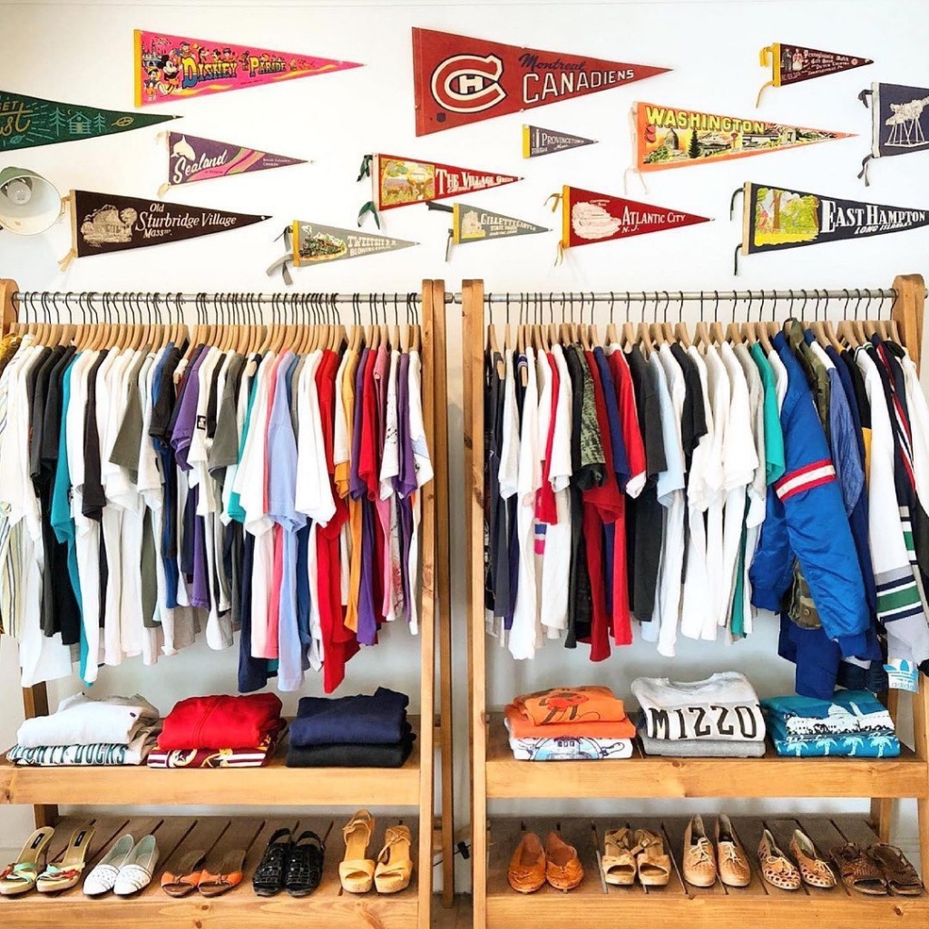 A rack of t shirts of various colors with vintage university pendants and vintage shoes.