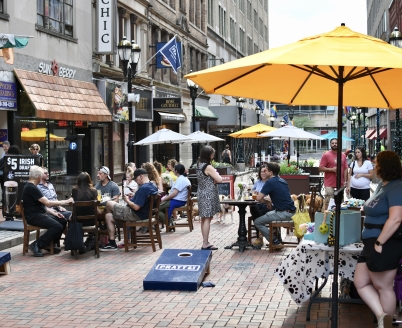 People sitting at tables on Pratt Street with cornhole boards in the foreground.