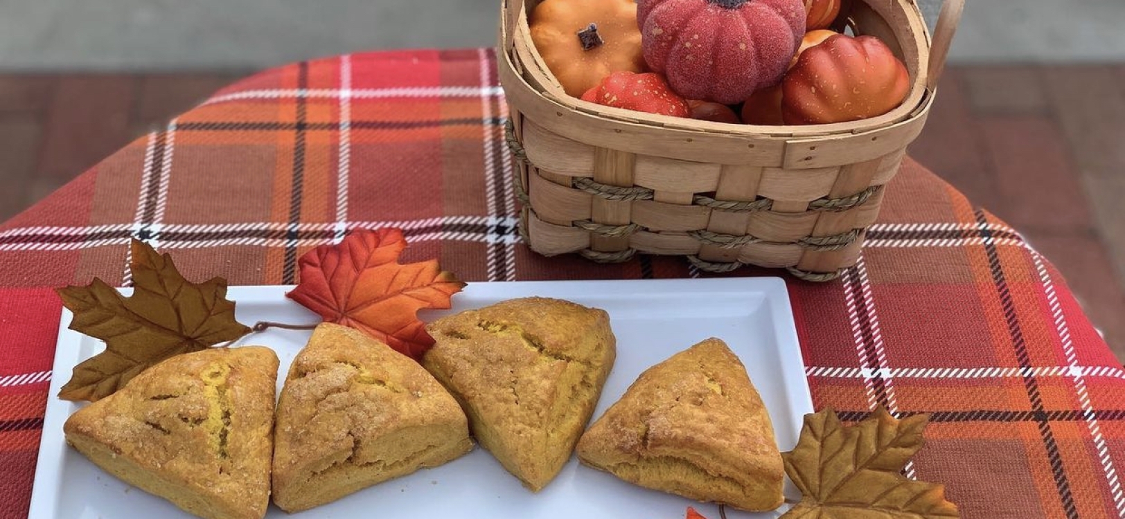 A plaid table stylized with leaves and small pumpkins with a plate of scones.